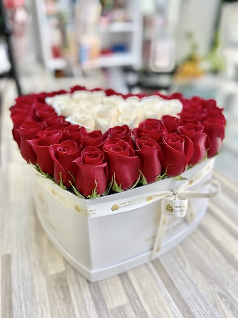 Heart-shaped white box filled with red roses around a cluster of white roses in the center
