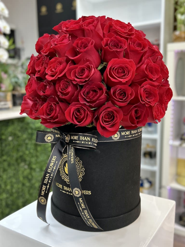 Round black hatbox filled with a dense dome of red roses and tied with a branded black ribbon