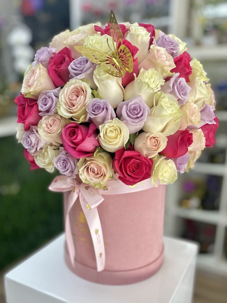 Round hatbox of pink, white, cream, and lavender roses with a gold butterfly accent and ribbon bow.