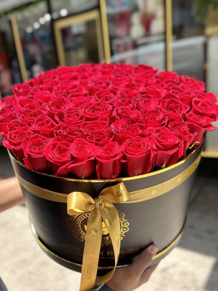 Large round hat box filled with tightly packed red roses and tied with a gold ribbon.