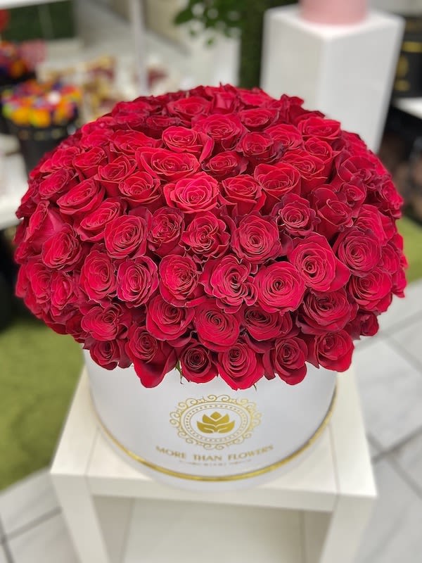 Large round box filled with tightly packed bright red roses on a white stand