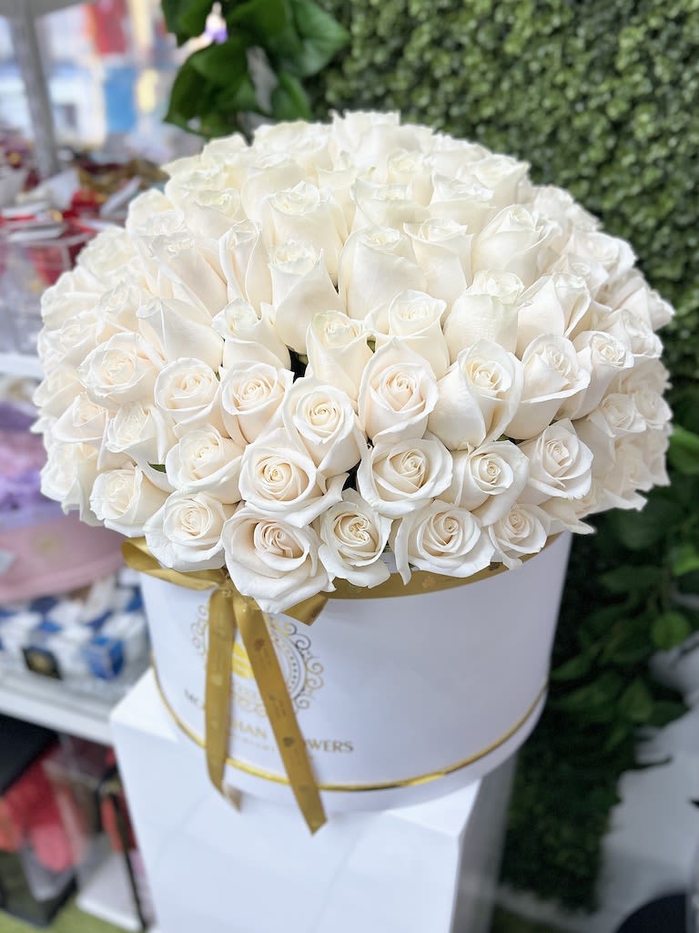 Large round hatbox of tightly packed white roses with a gold ribbon around the box