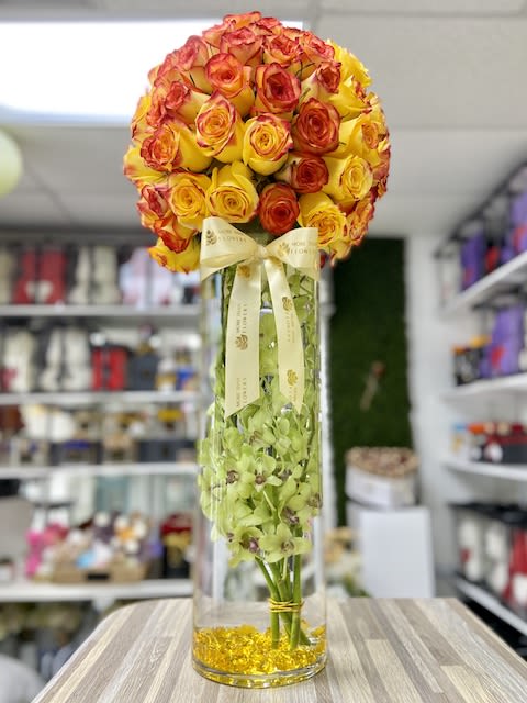 Tall glass vase with yellow and orange rose sphere and green orchids inside the vase