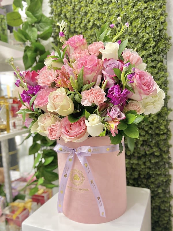Round pink hatbox filled with pink, white, and purple mixed roses and carnations.