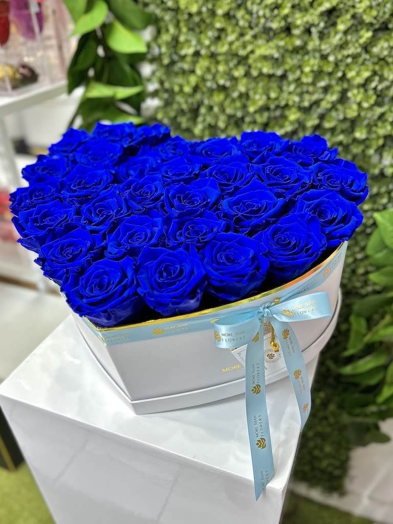 Heart-shaped box of vivid blue roses with a ribbon on a white pedestal