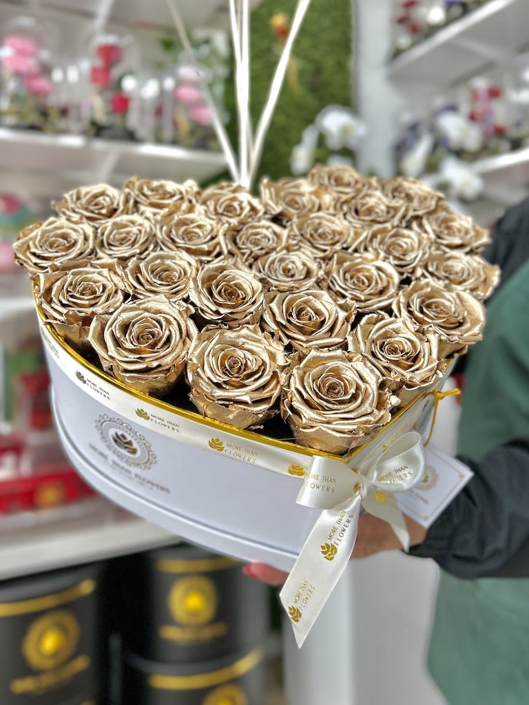 Heart-shaped white box filled with metallic gold roses and tied with a white logo ribbon