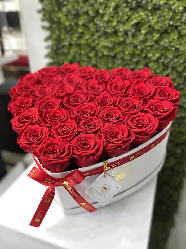 Heart-shaped white box filled with tightly packed red roses and a red ribbon bow.