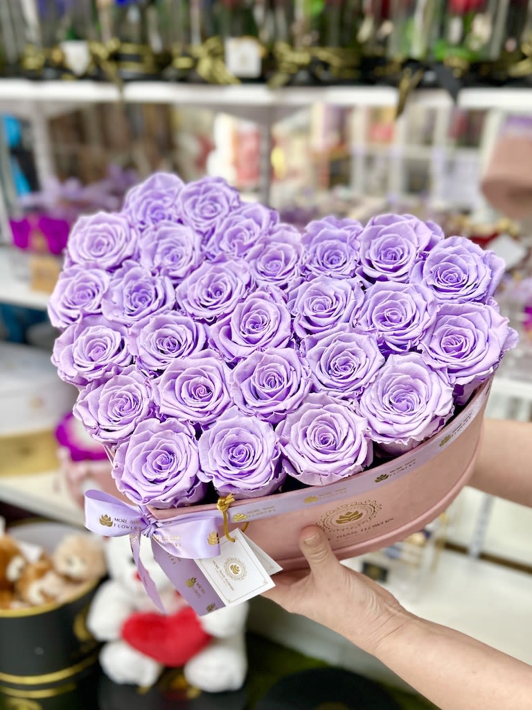 Heart-shaped box filled with tightly packed lavender roses held in both hands