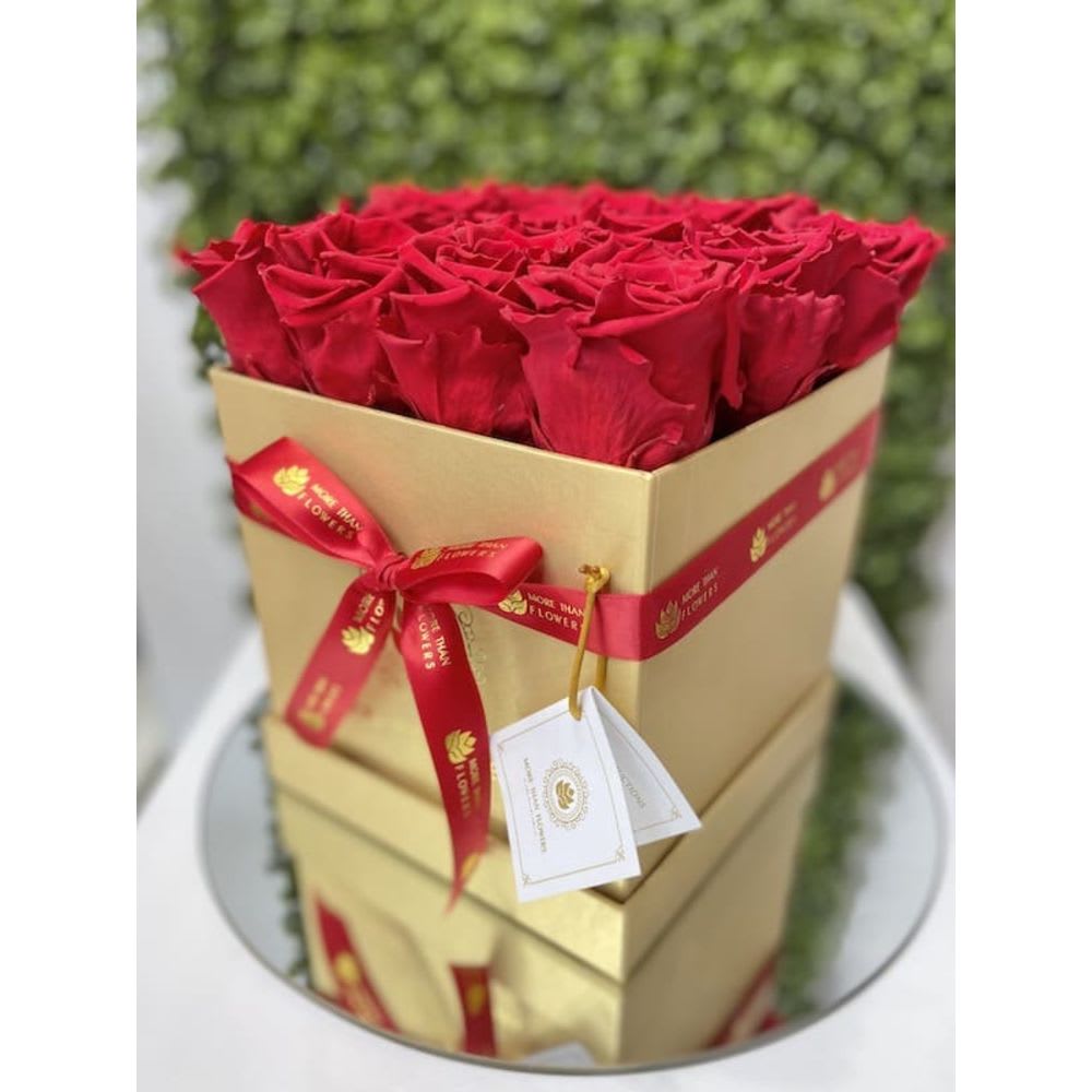 Square gold box filled with tightly packed red roses and tied with a red ribbon.