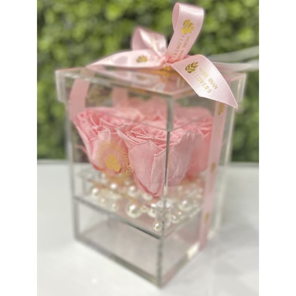 Pink roses arranged in a clear acrylic box with pearl beads and a pink ribbon bow