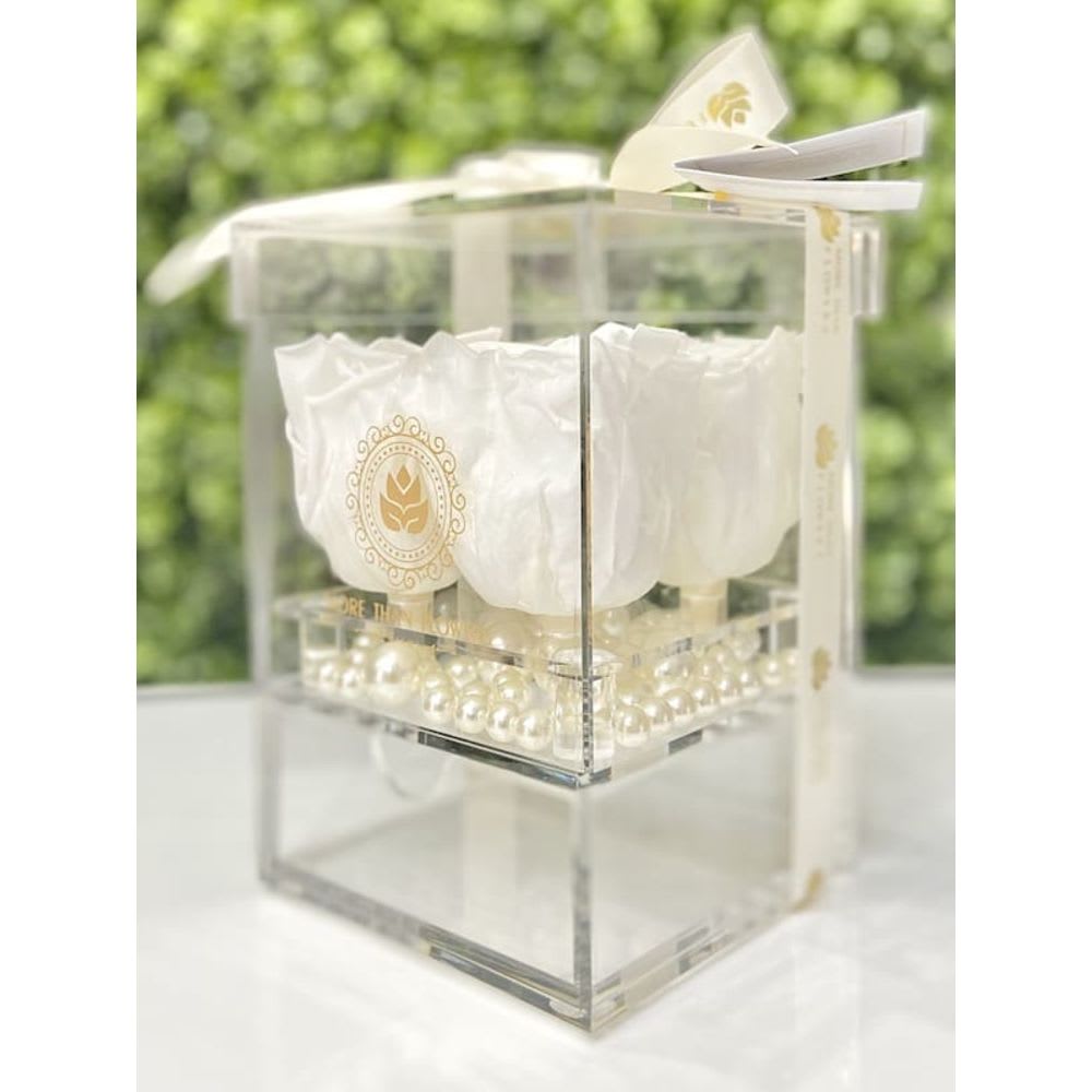 White roses arranged in a clear acrylic cube box with pearl accents and ribbon