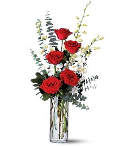 Red roses in a clear glass vase with white filler flowers and tall greenery