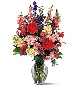 Mixed bouquet of red, pink, yellow, and purple flowers in a clear glass vase