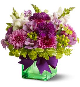 Purple and pink mixed bouquet in a green glass vase with a ribbon