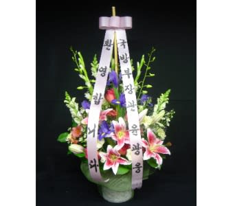 Tall floral arrangement with pink lilies and purple flowers in a pot, accented by long Korean message ribbons.