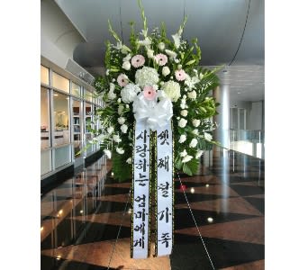 Large standing sympathy spray with white and pale pink flowers and long message ribbons on an easel.