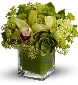 Green floral arrangement in a square glass vase with white orchids and roses