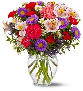 Mixed bouquet of pink, purple, and red flowers in a clear glass vase