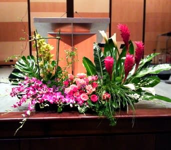 Wide pink and white tropical floral arrangement displayed in front of a wooden podium