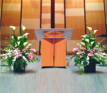 Two large floral arrangements with white calla lilies and pink flowers flanking a wooden podium.