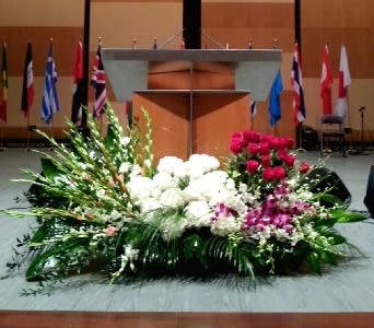 Large stage floral spray with white blooms, red roses, and purple orchids arranged in front of a podium