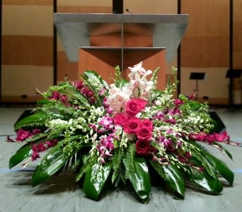 Large pink and white floral arrangement displayed in front of a podium on a stage