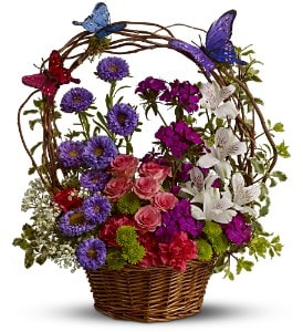Basket arrangement of mixed pink, purple, and white flowers with butterflies on a vine arch
