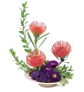 Modern arrangement of orange pincushion protea and purple flowers in a low ivory dish