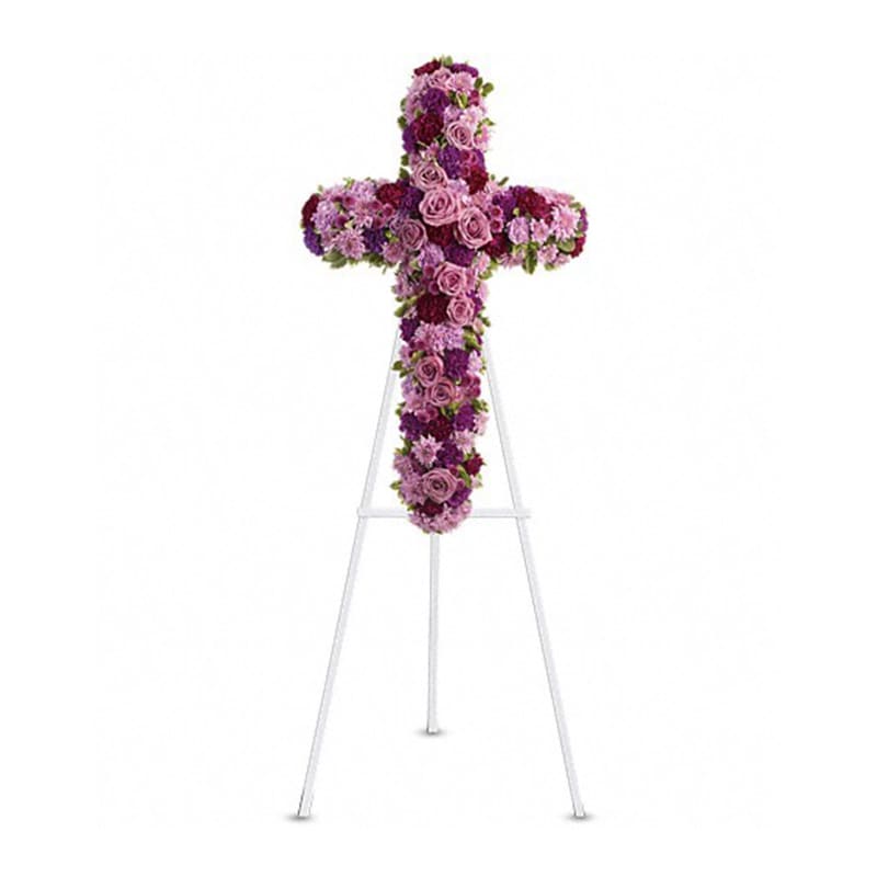 Standing floral cross of pink and purple blooms displayed on a white easel.