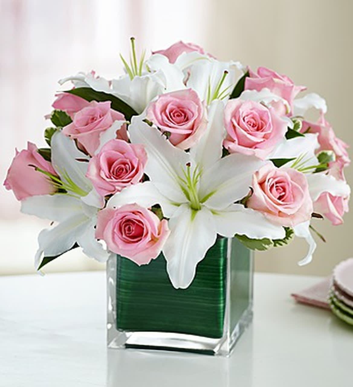 Pink roses and white lilies arranged in a clear square vase