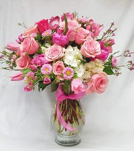 Pink roses and small white flowers in a glass vase with a pink ribbon