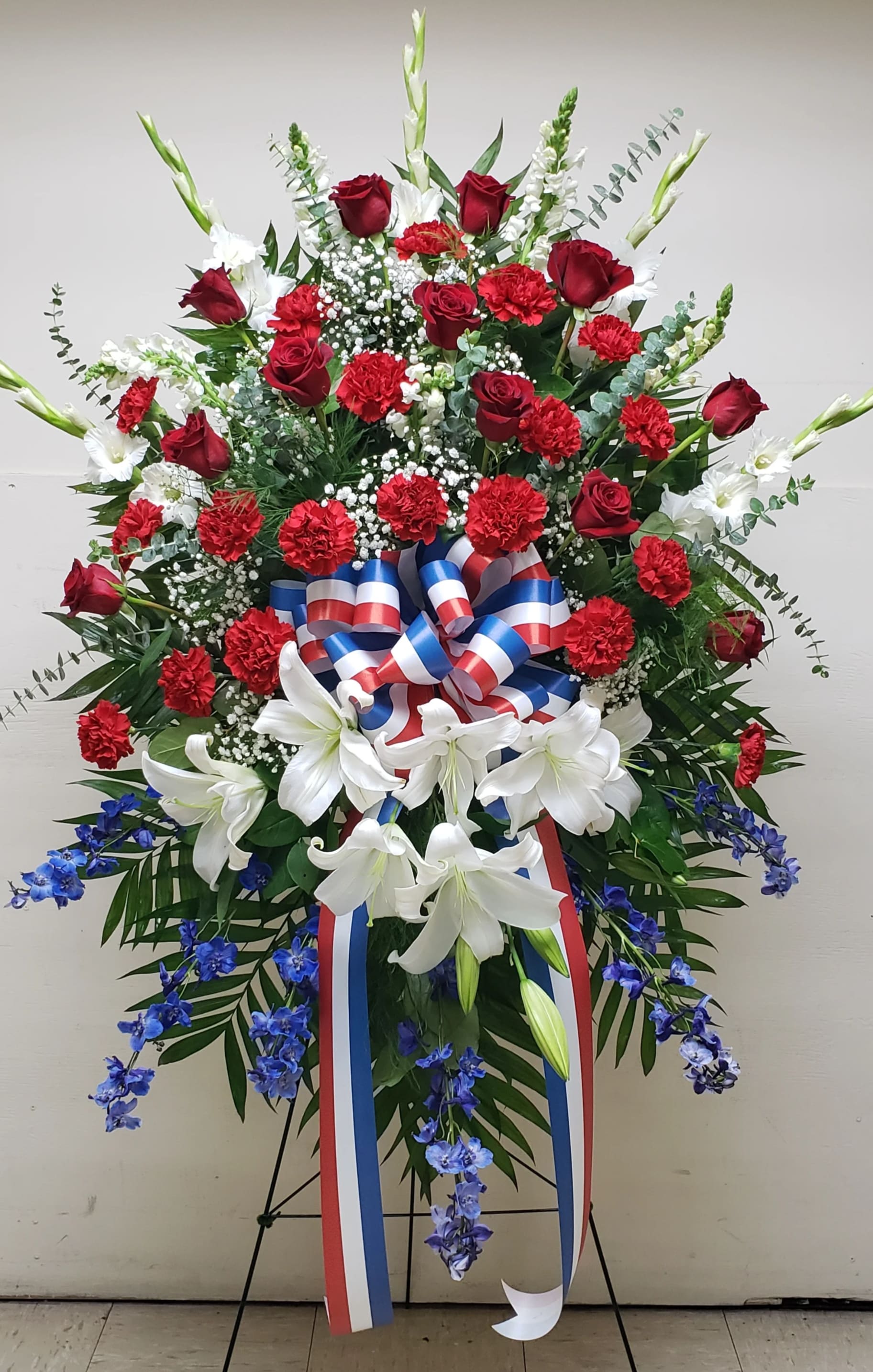 Tall red, white, and blue standing spray with roses, carnations, lilies, and ribbon on an easel
