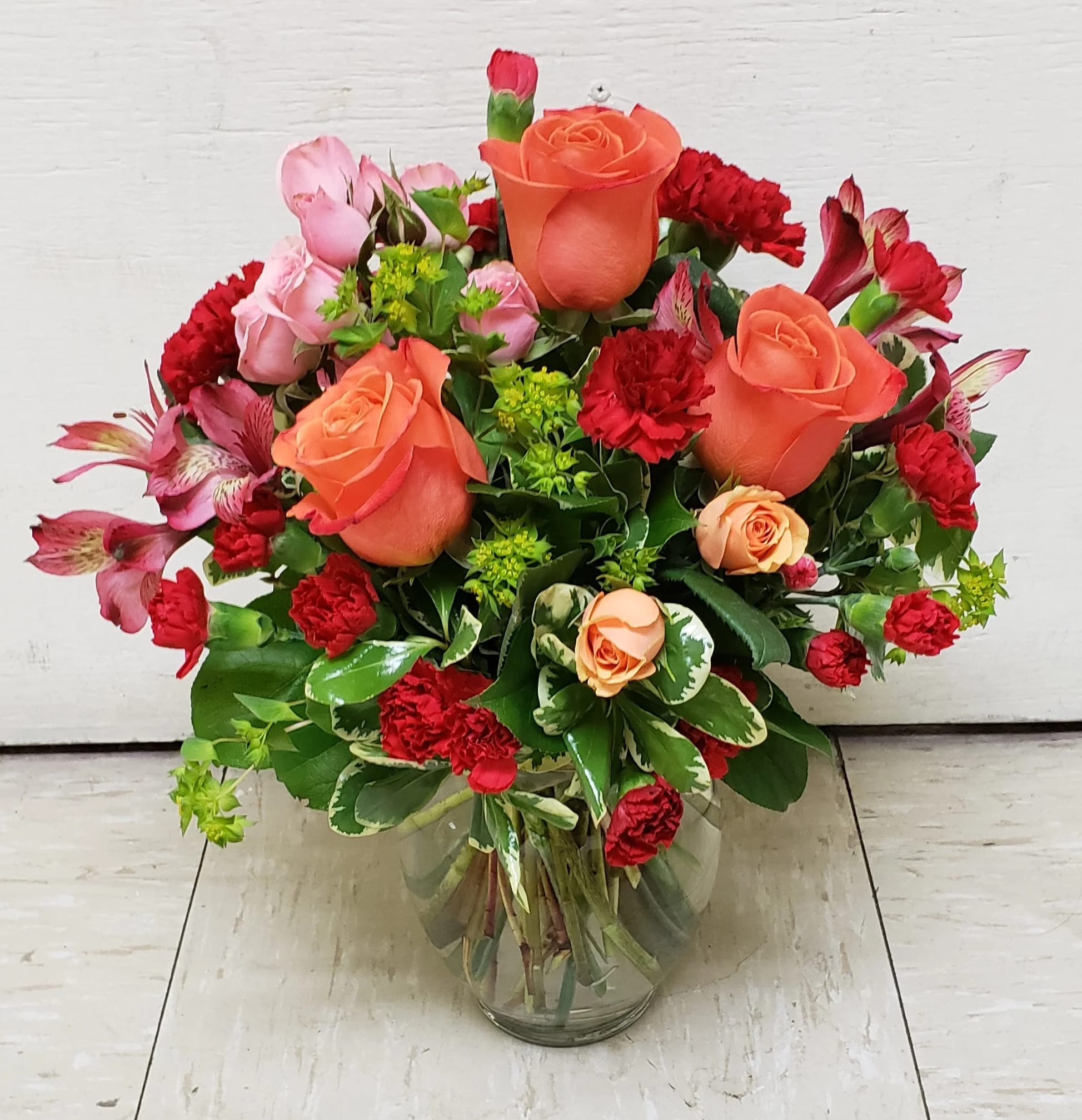 Bouquet of orange roses, red carnations, and pink alstroemeria in a glass vase