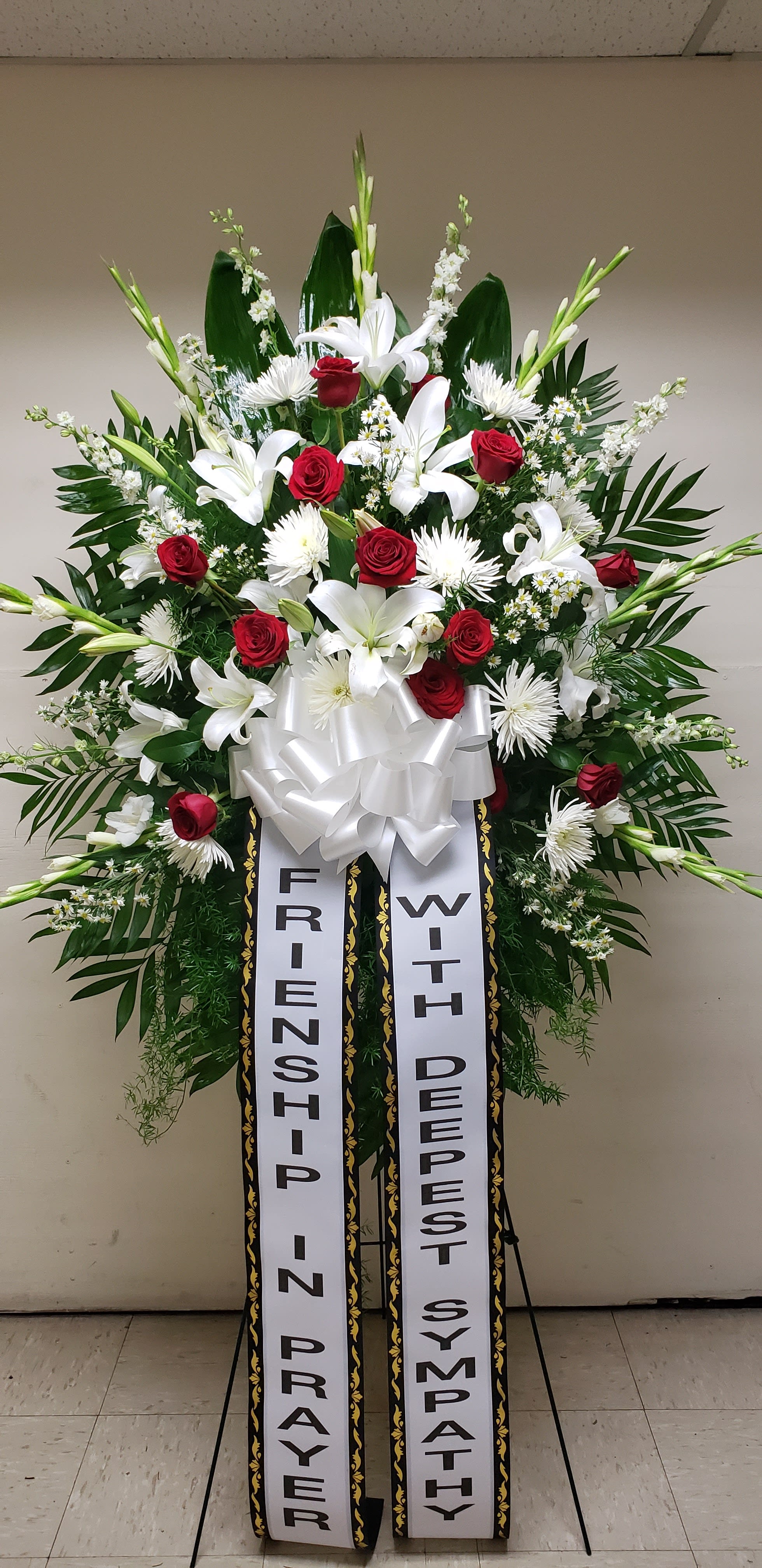 Standing sympathy spray with red roses, white lilies, and ribbon banners