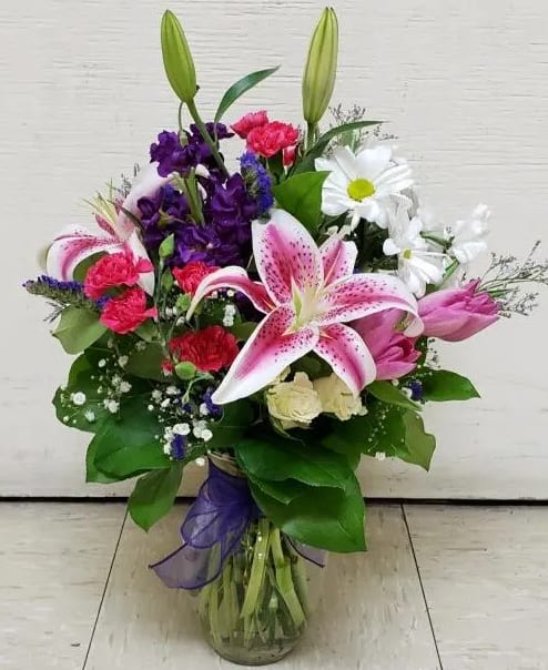 Bouquet of lilies, daisies, carnations, and purple flowers in a glass vase