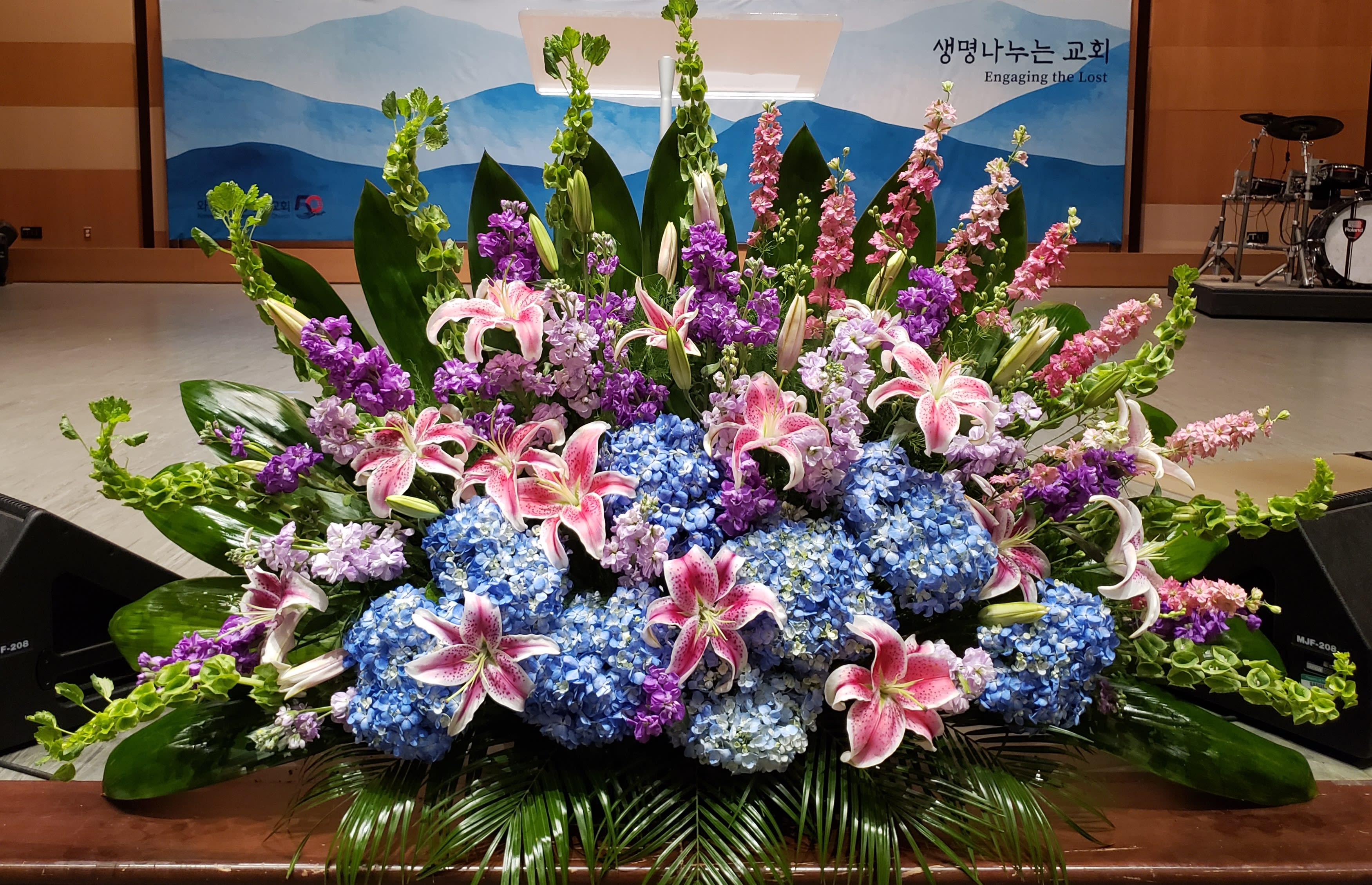 Large floral arrangement with pink lilies, blue hydrangeas, and purple flowers