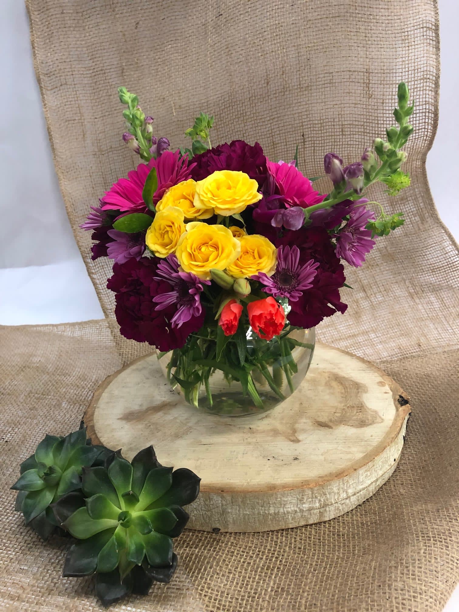 Mixed bouquet of yellow, pink, and purple flowers in a clear glass vase