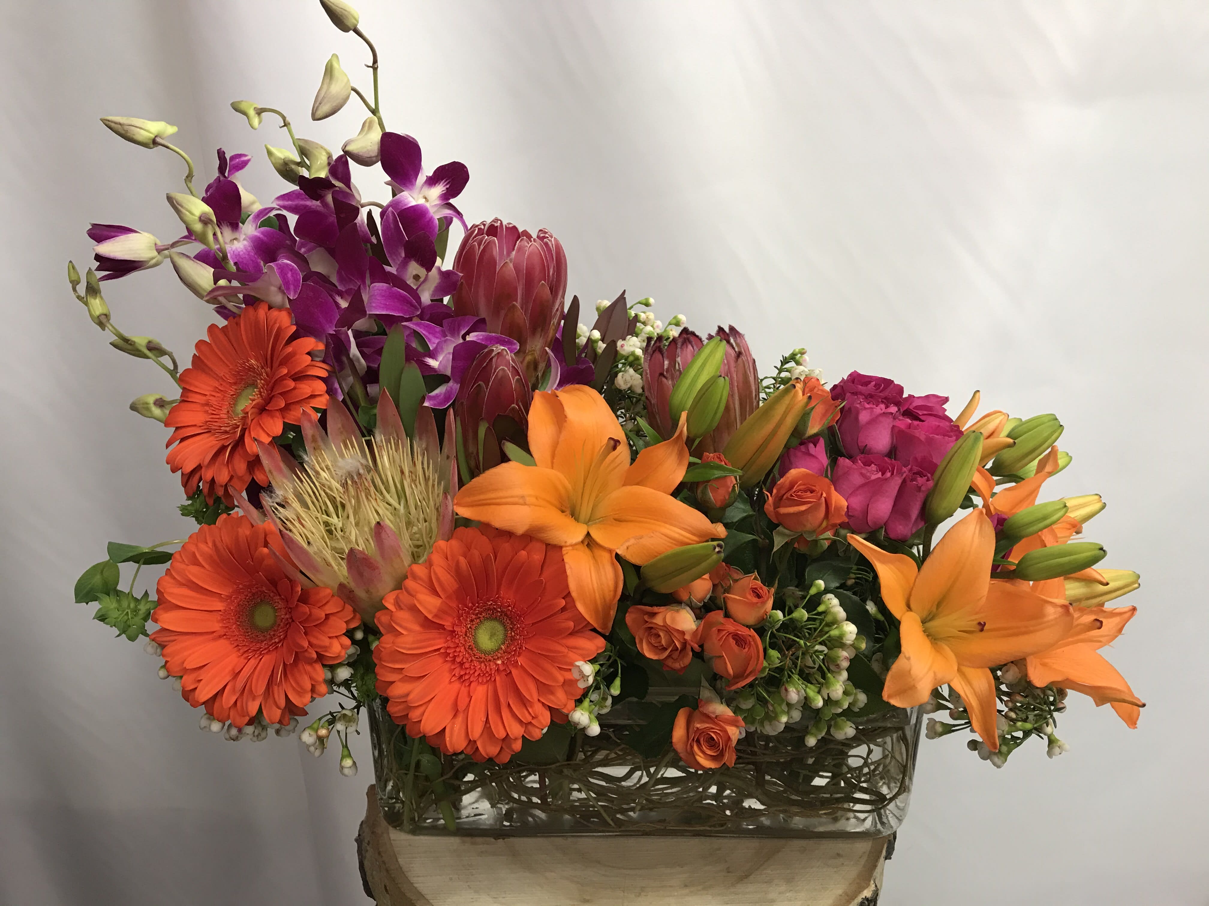 Bright mixed bouquet with orange lilies, gerbera daisies, and purple orchids in a glass vase