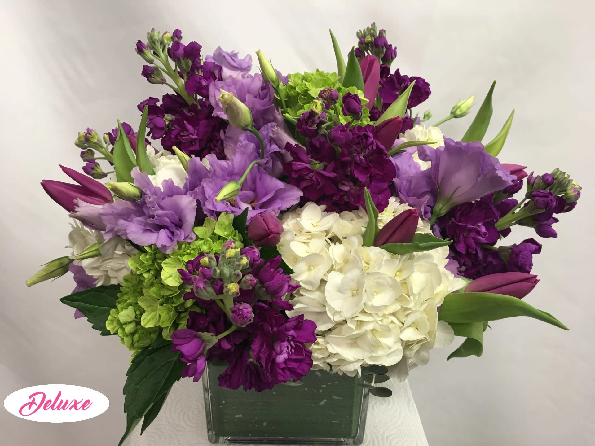 Purple and white floral arrangement in a square glass vase
