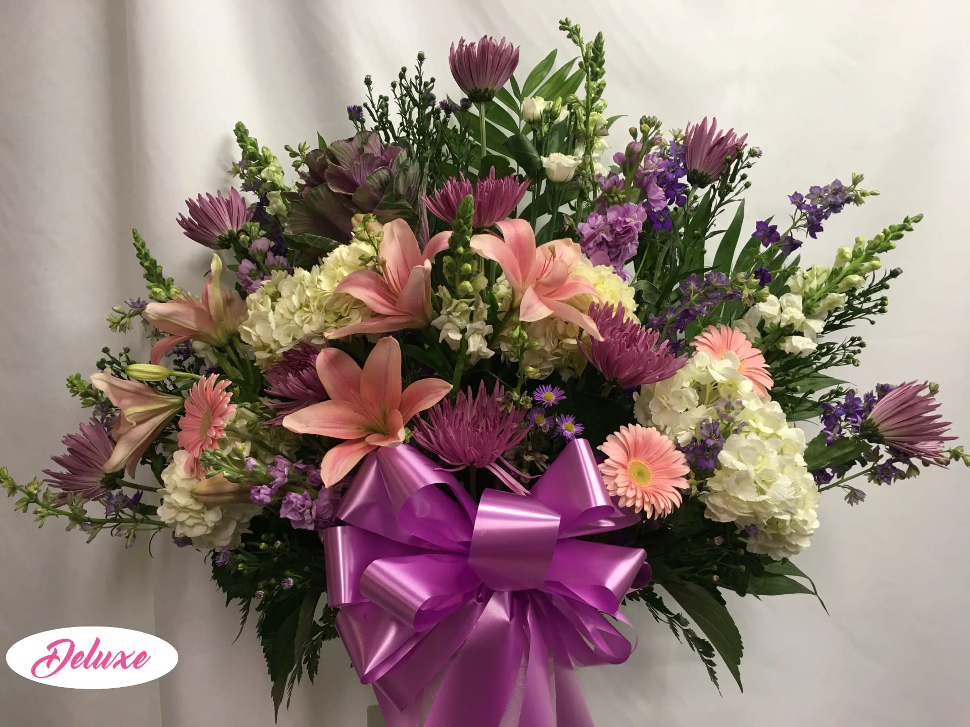 Large bouquet of pink lilies, purple flowers, and white hydrangeas with a purple bow