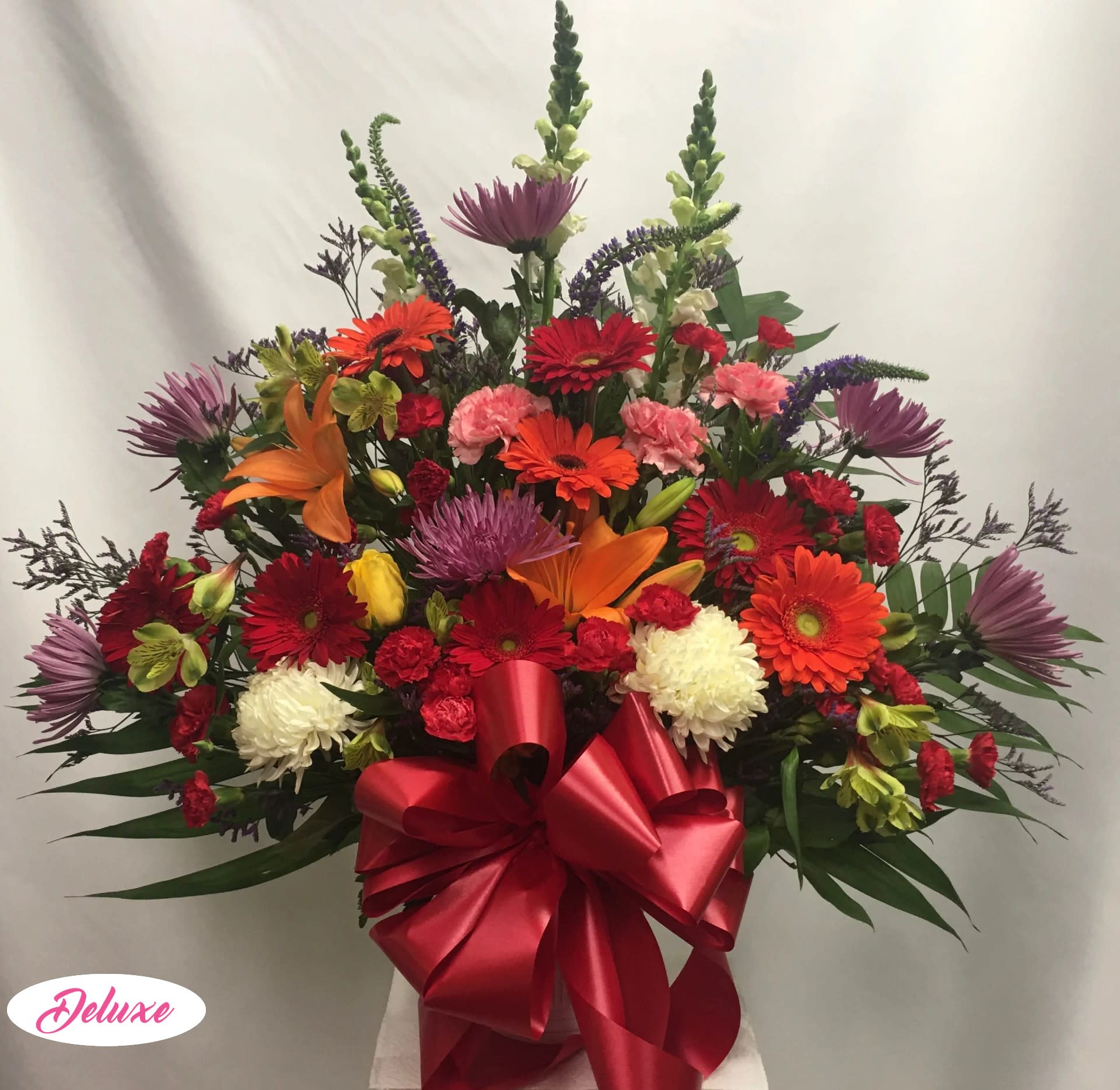Large mixed bouquet with gerbera daisies, lilies, and a red ribbon bow