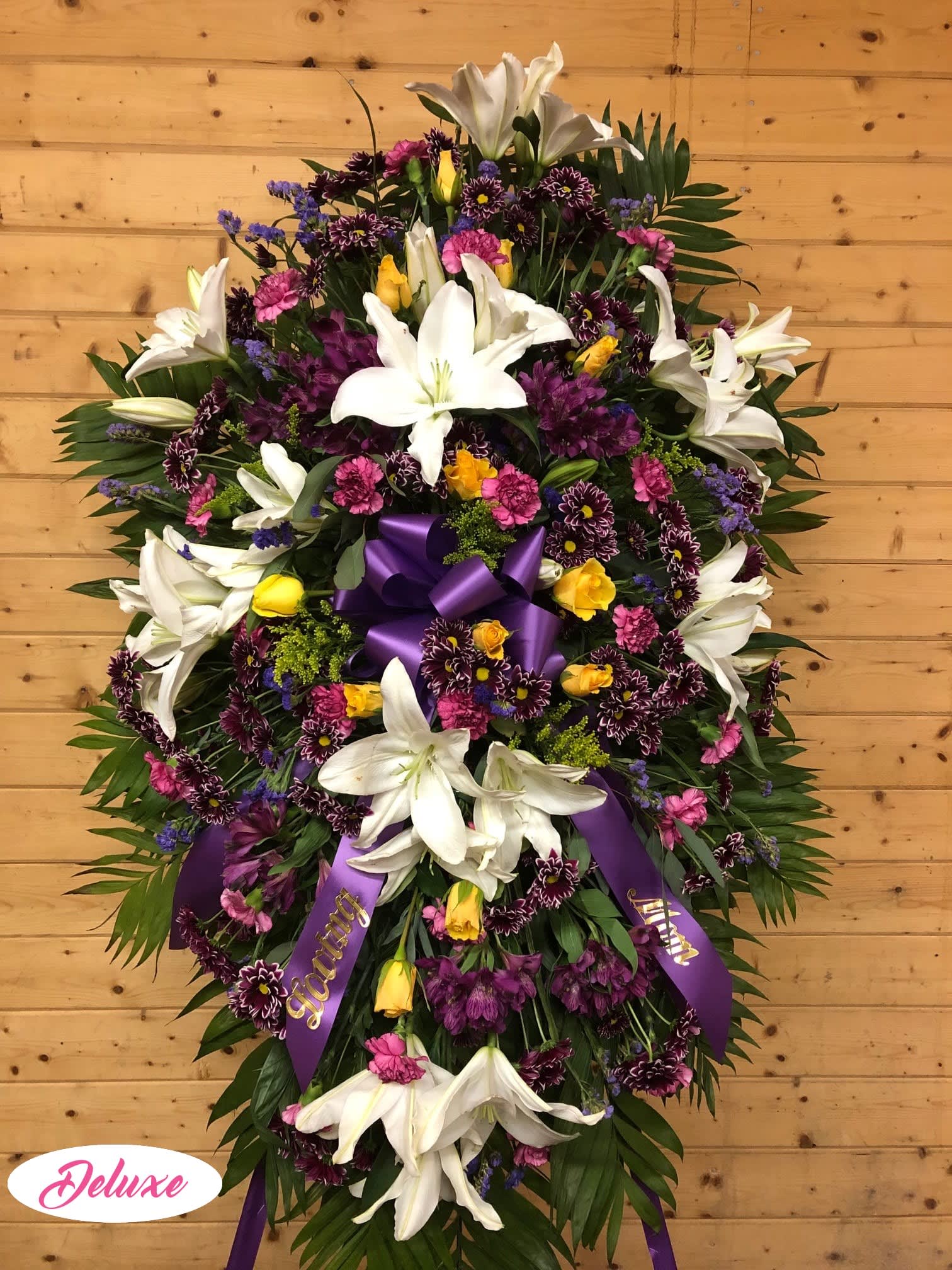 Large standing floral spray with white lilies, purple and pink flowers, and a purple ribbon
