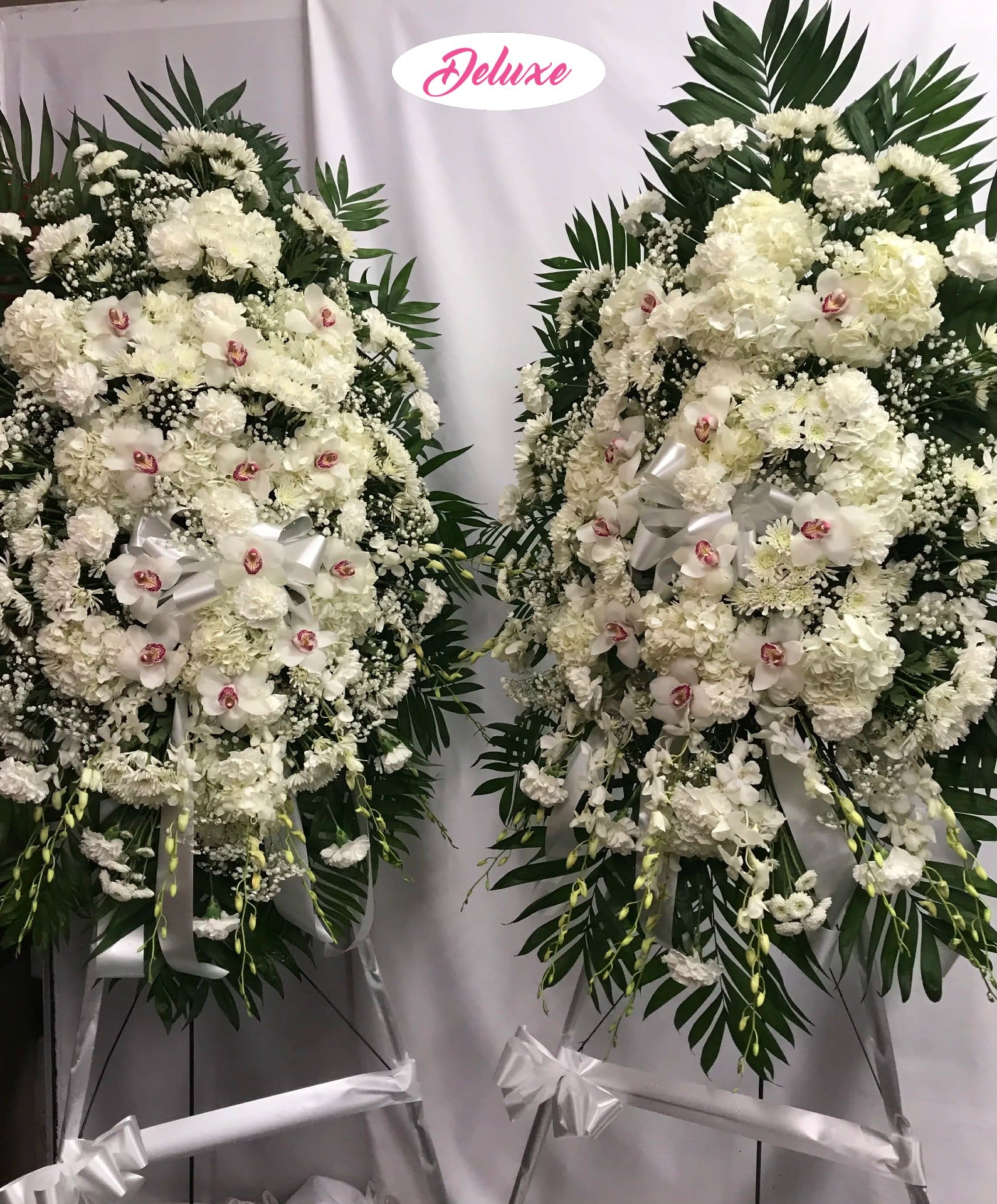 Two large white floral standing sprays with ribbons and dark green foliage