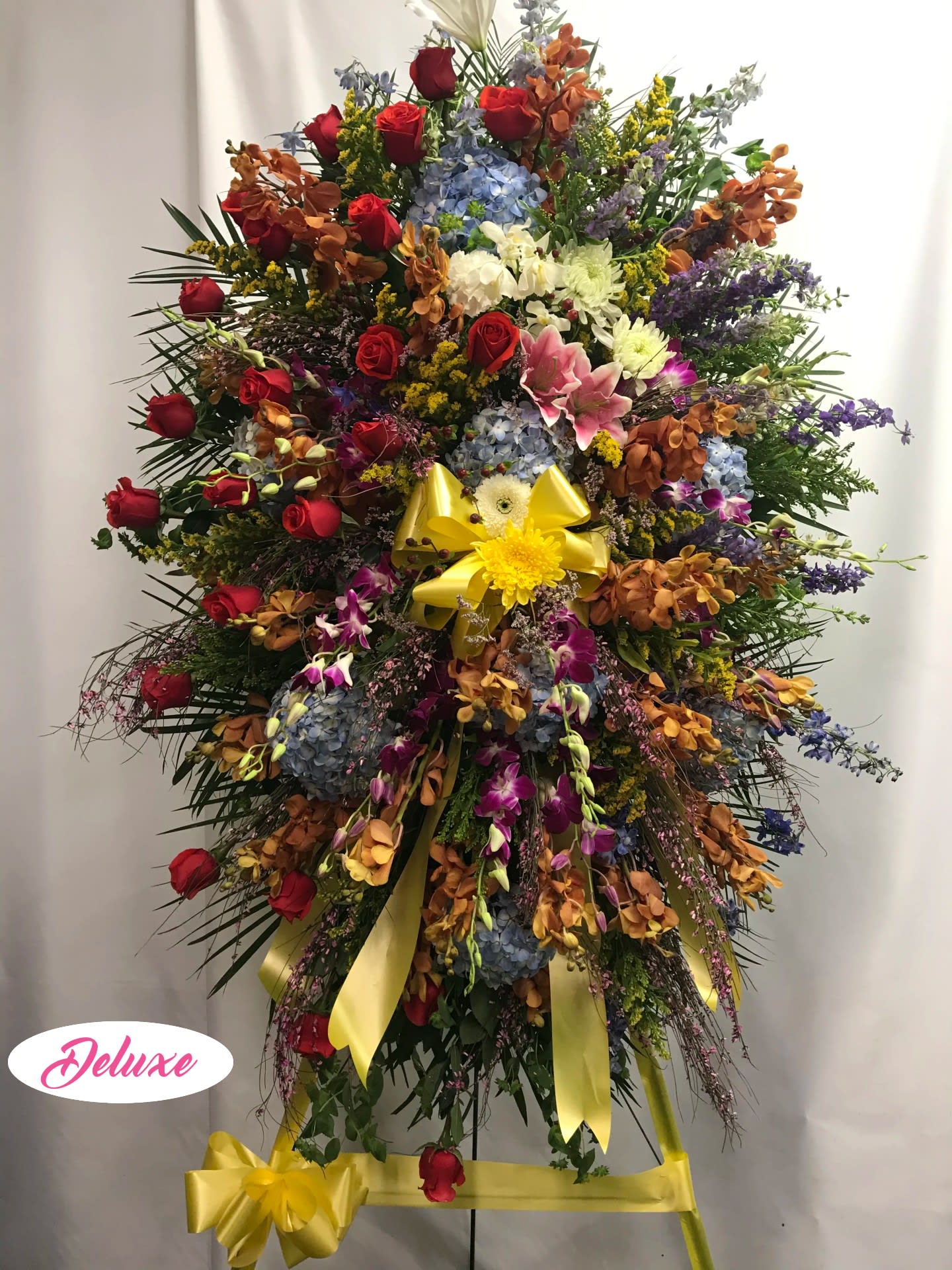 Large standing spray with red roses, blue hydrangeas, and yellow ribbon