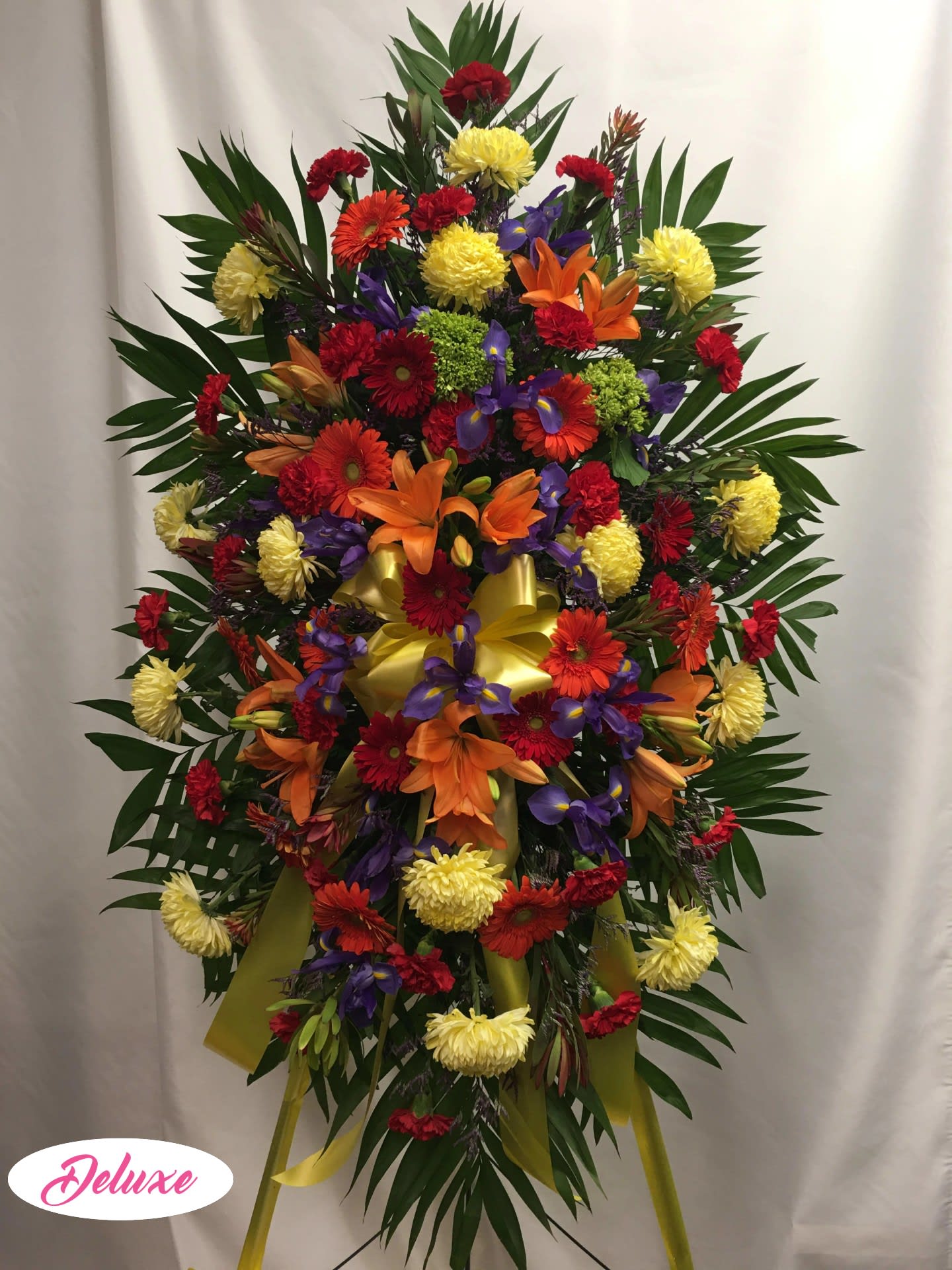 Large standing spray with mixed bright flowers and a yellow ribbon