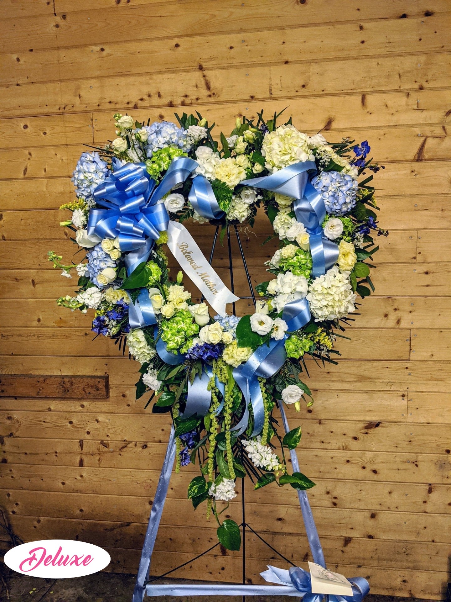 Heart-shaped floral wreath with blue ribbons on a stand