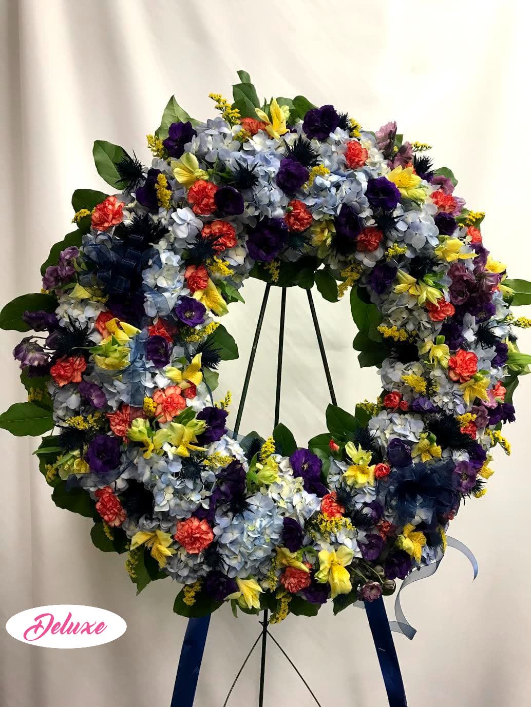 Large floral wreath on a stand with blue, purple, yellow, and coral flowers