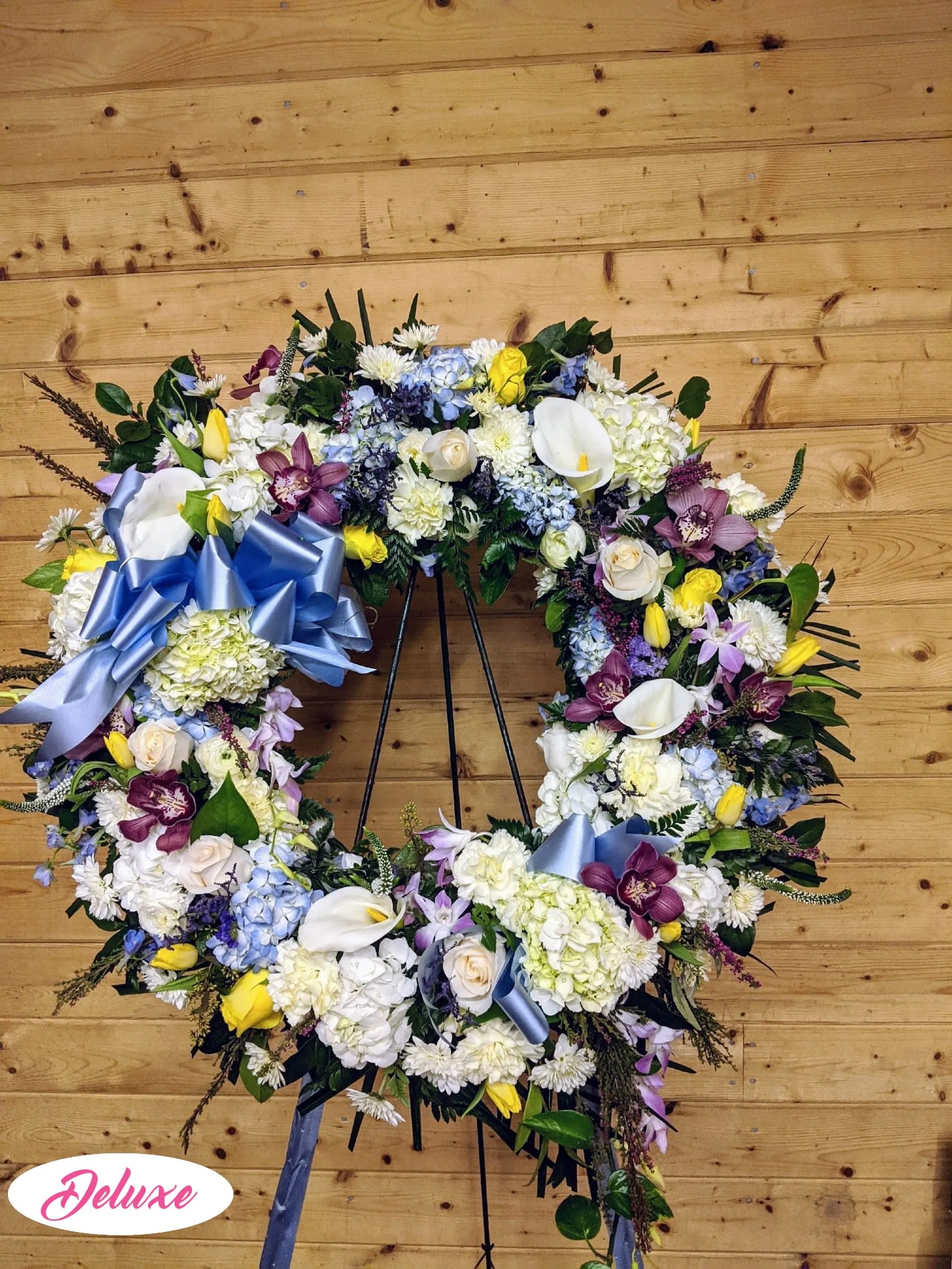 Large floral wreath with mixed blooms and blue ribbon on a stand
