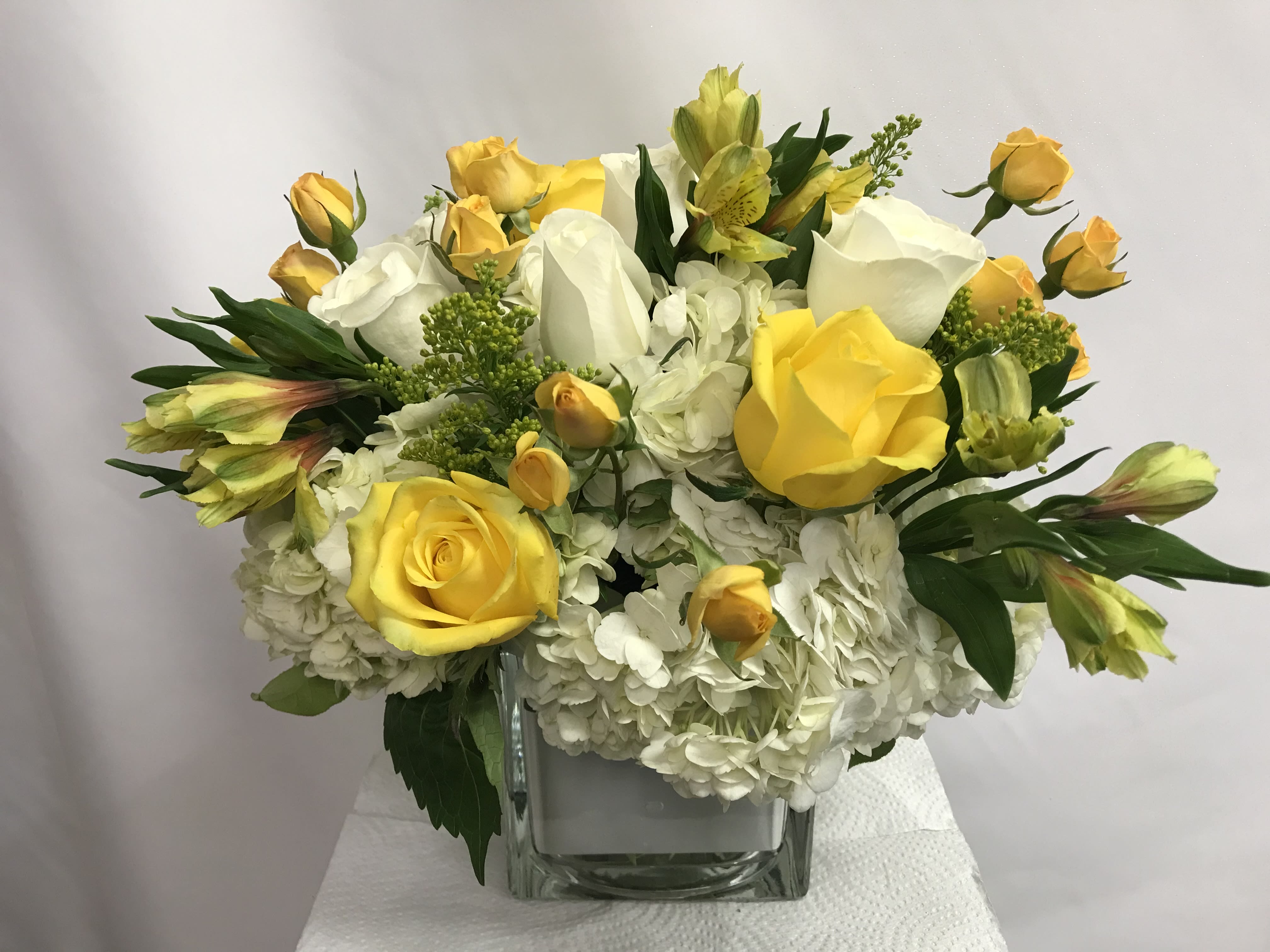 Yellow and white rose bouquet in a clear square vase