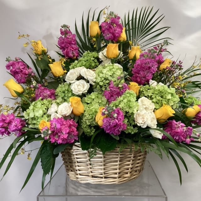 Basket arrangement with yellow roses, white roses, pink flowers, and green hydrangeas